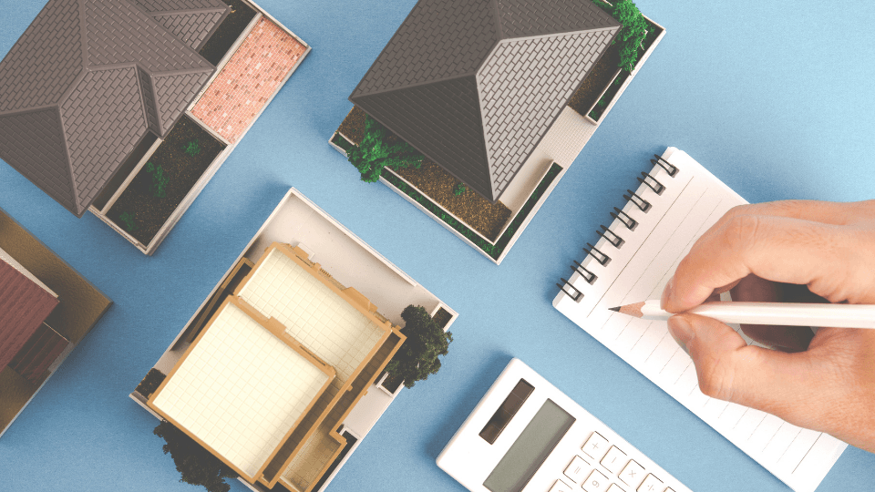 Person writing on note pad with calculator and small homes around