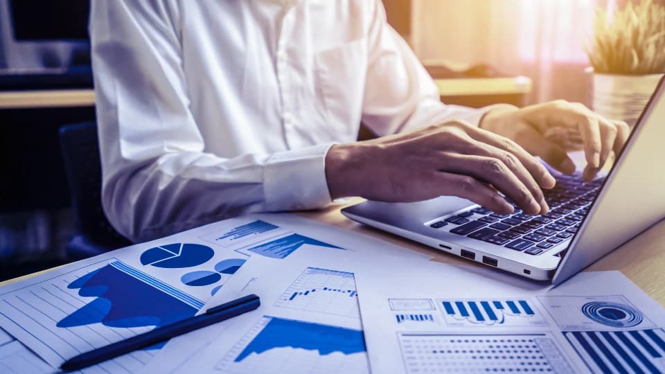 man typing on computer with graphs on desk
