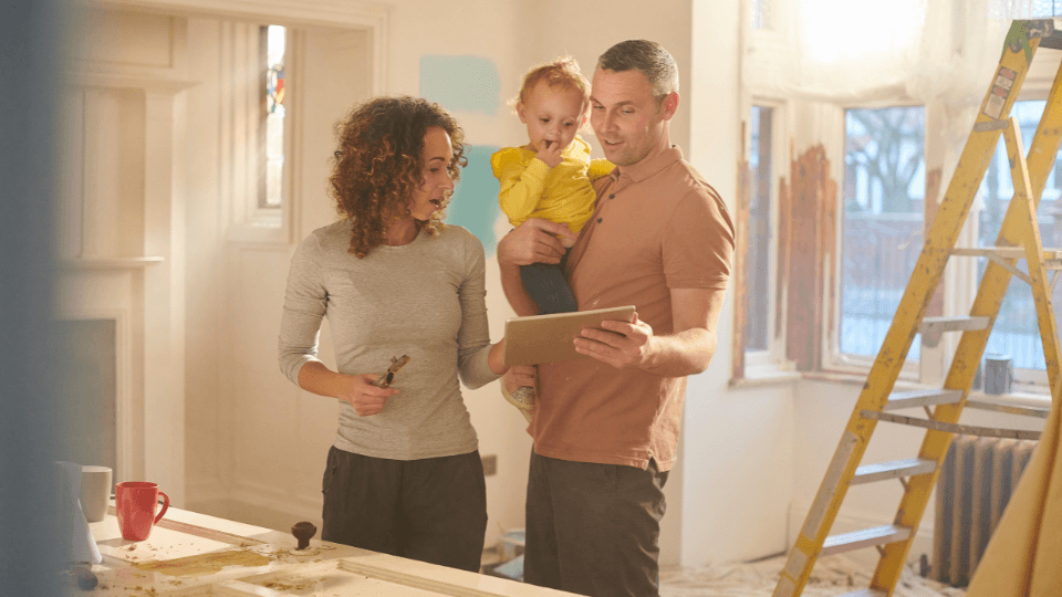 A man and woman holding a baby looking at a notebook