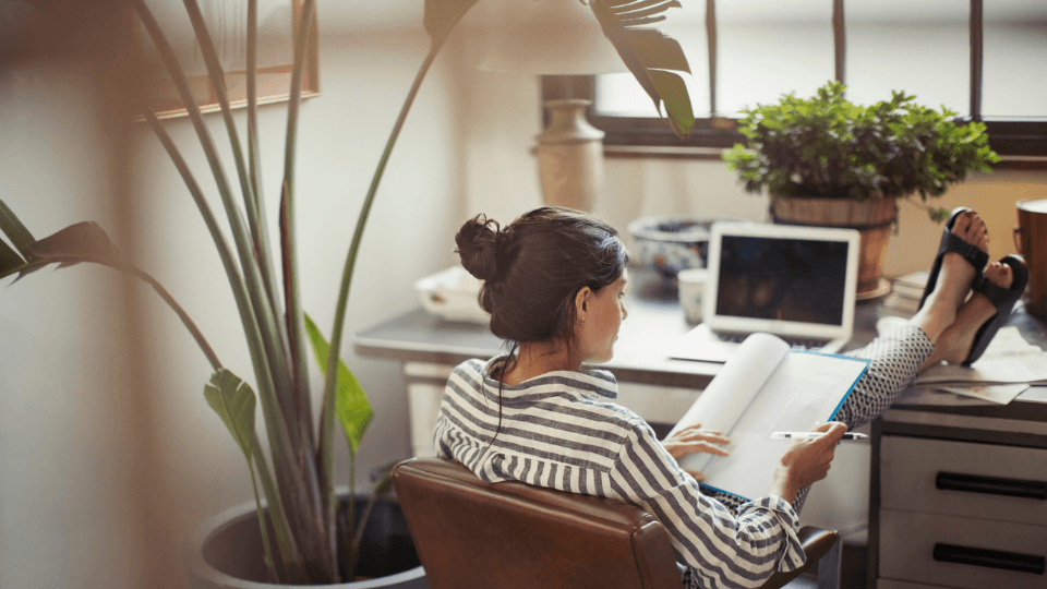 Woman sitting in a desk chair with feet on desk and writing in a book