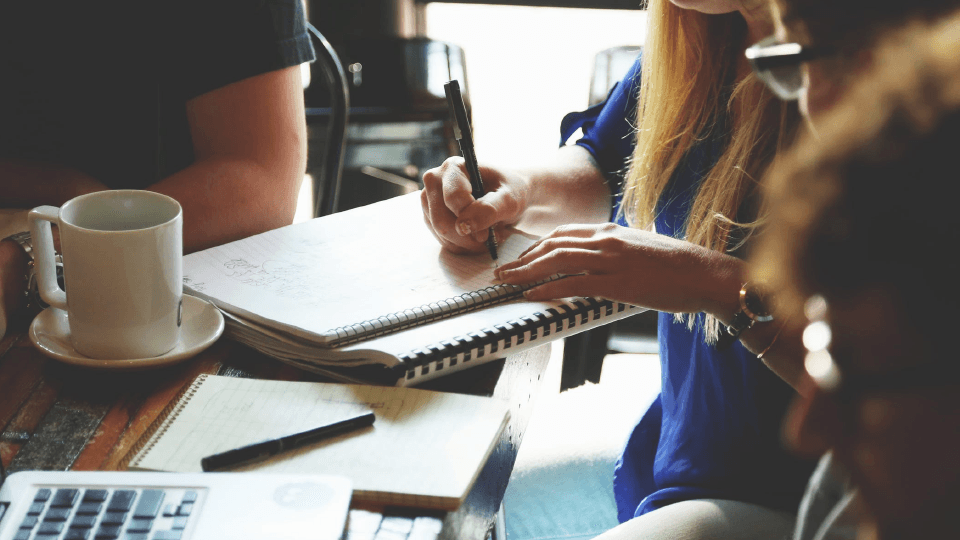 People works at the table with notebooks, laptop and coffee mug