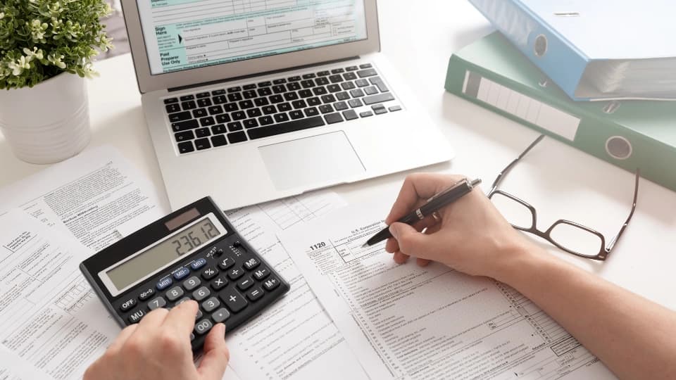 person writing on paper and typing on calculator