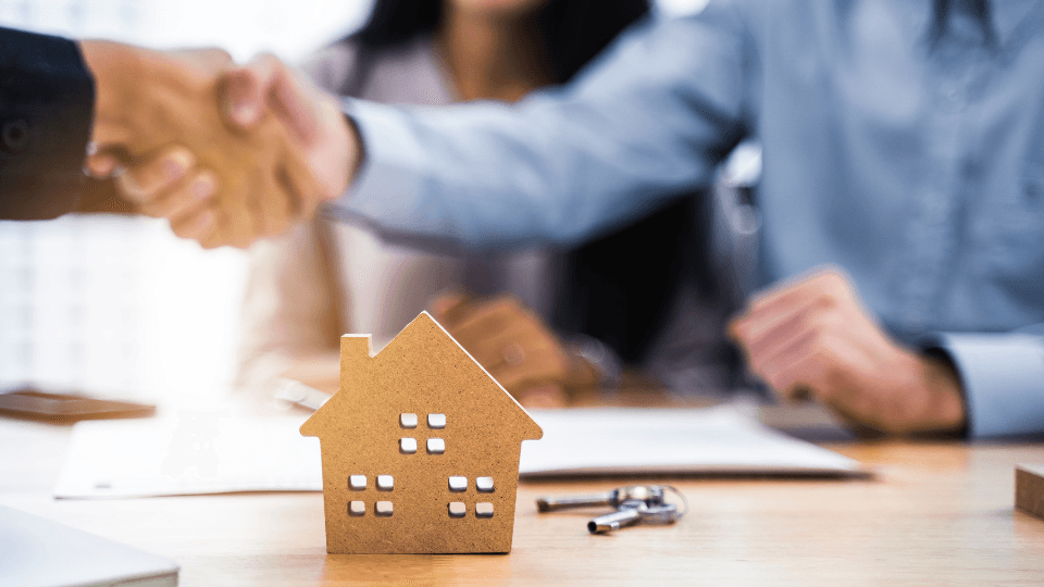 Two people shaking hands with a house in front of them