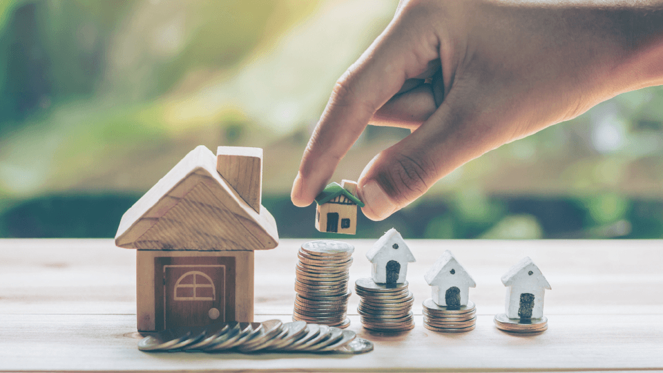 Miniature wooden houses standing on different height coin piles