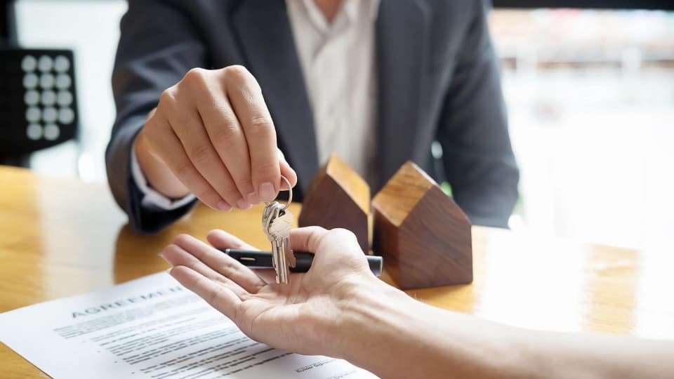 Real estate agent holding house key to his client after signing contract