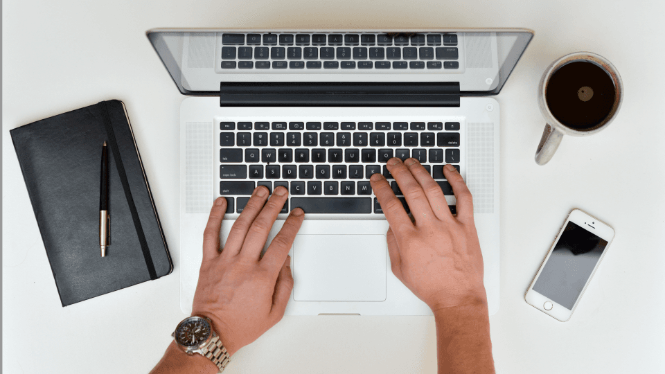 Man working on laptop and note, pen, smartphone, coffee mug next to him