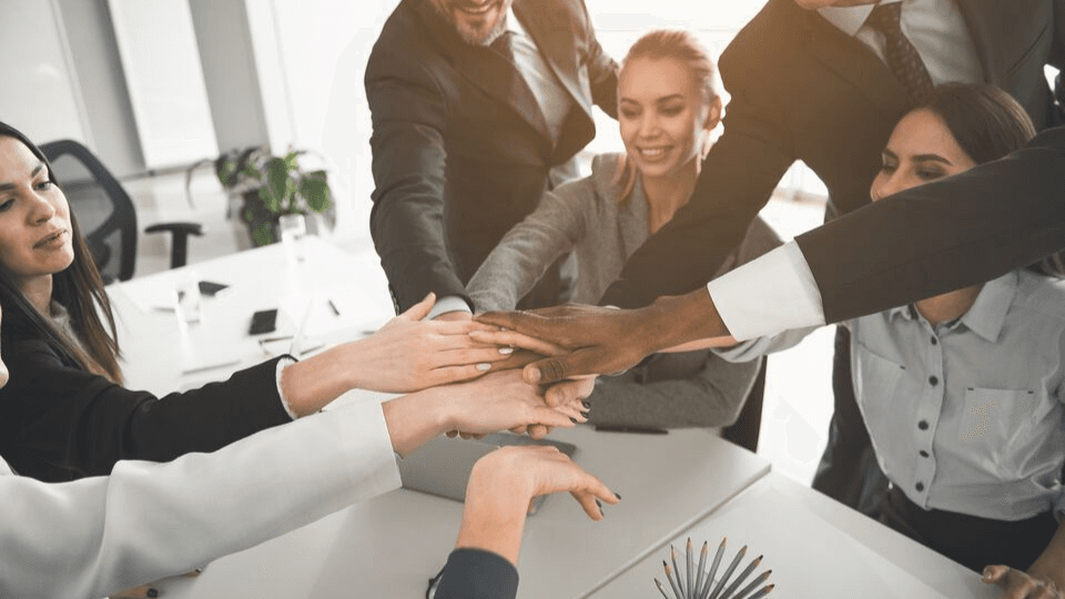 Team of people in a room wearing business attire putting their hands together