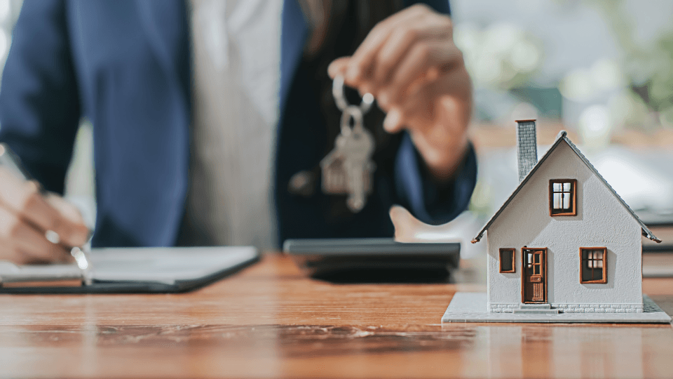 Man holding keys behind a desk with a small house model on top