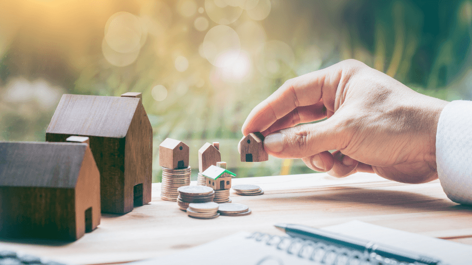 Man's hand holding small house on a stack of coins