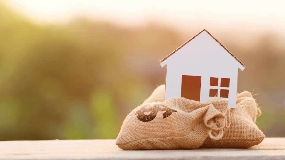 Miniature wooden house standing on the small money bag