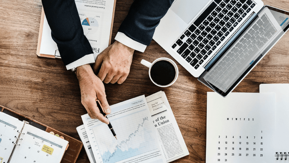 Man sitting at the desk with laptop and coffee and pointing to graphs