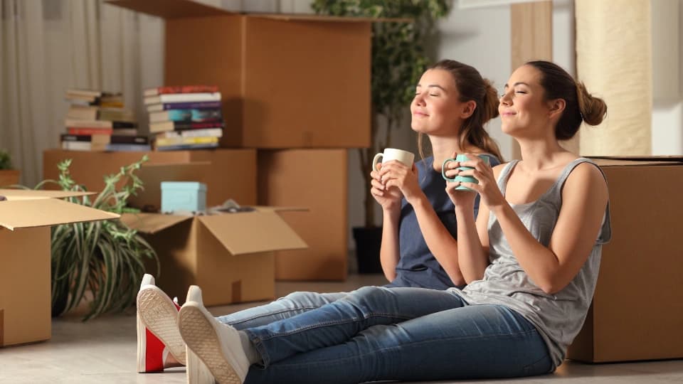 Two girls sitting on the floor around moving boxes