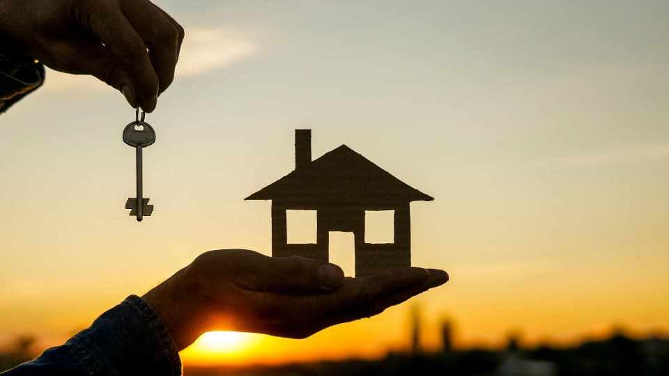 person holding a house and key while sunset