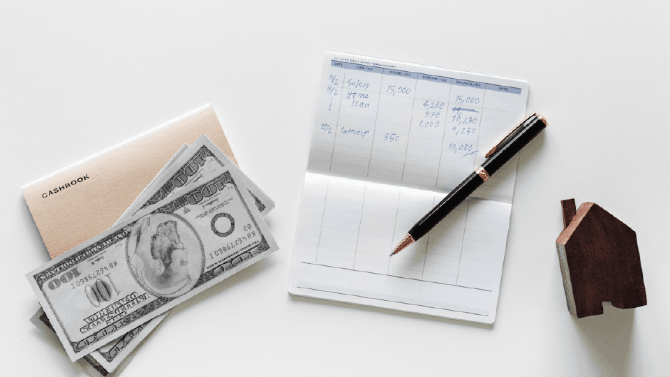 Several 100 bills, Checkbook, Pen, Miniature house on white background
