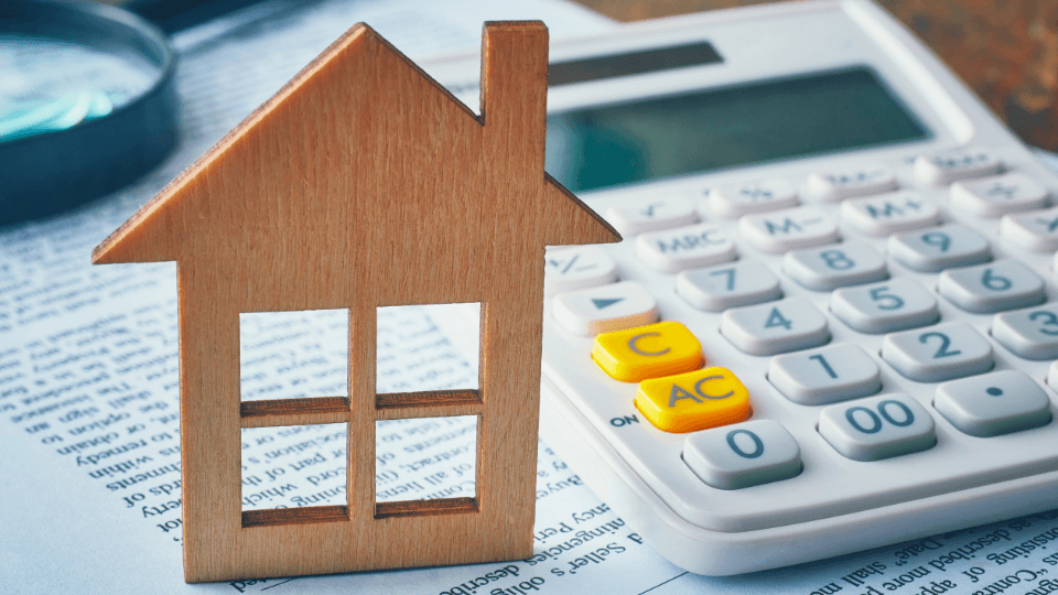 Wooden house on a stack of papers with a calculator