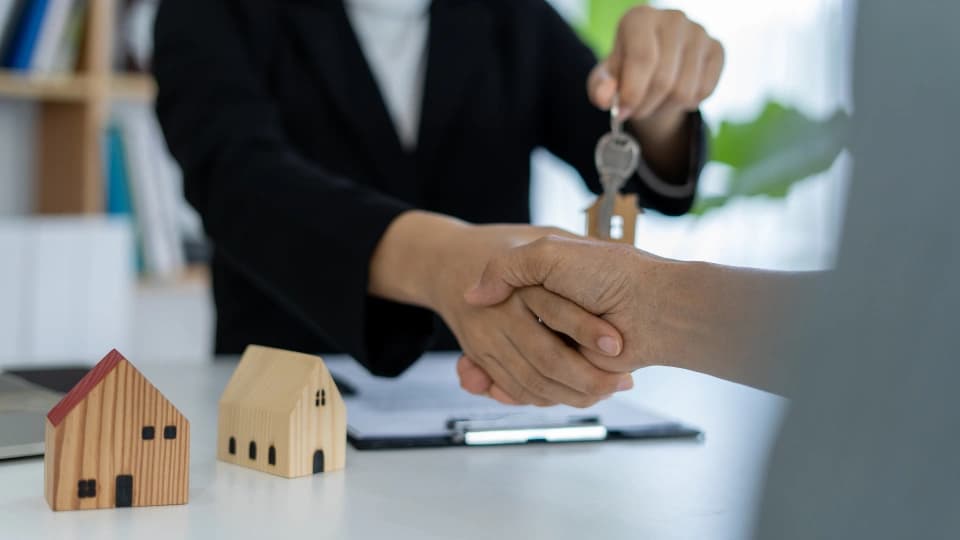 Real estate professional shaking hands and delivering keys to new homeowners