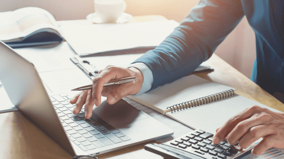 Man working on laptop with calculator, notebook and pen