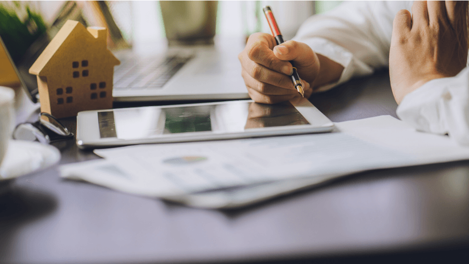 Man hands with stilo and graphs, tablet, house model and laptop on a table
