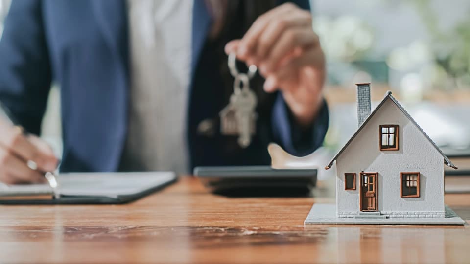 Man holding key with a model house on a desk