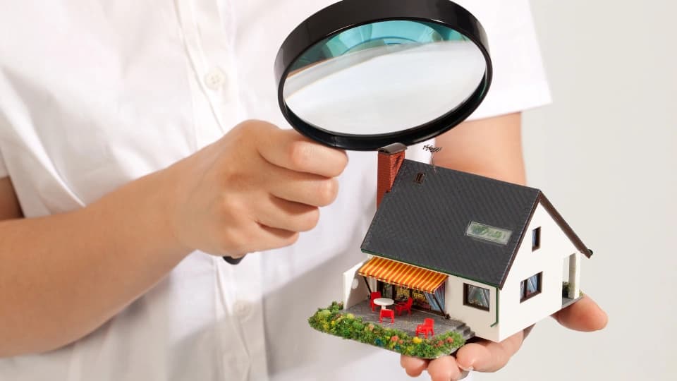 Person holding a magnifying glass looking at a house