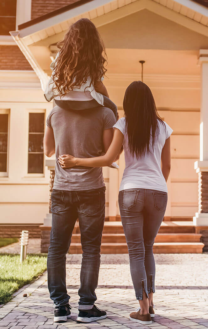 A family walking into a home. They have a child and she is on the dad's shoulders.